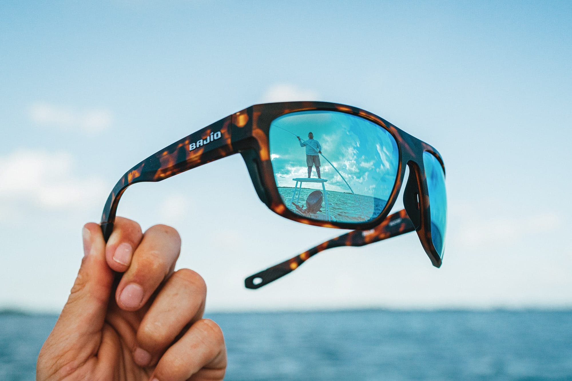 Bajio polarized sunglasses held up against ocean backdrop